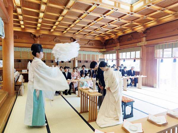 神社での神前結婚式にて、神職が大麻（おおぬさ）を振って新郎新婦を祓い清めている様子