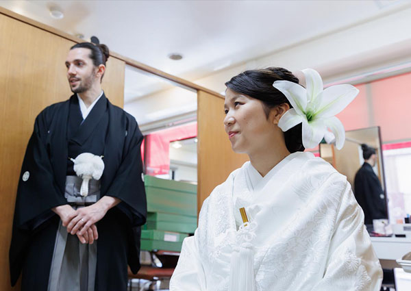 百合の髪飾りをつけた白無垢の花嫁と、紋付袴姿の外国人新郎の記念写真。