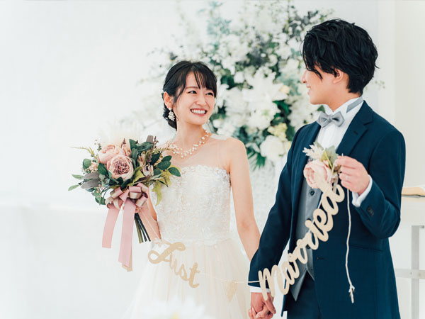 披露宴会場で「Just Married」のガーランドを手に持ち、見つめ合って微笑むウェディングドレス姿の新婦とタキシード姿の新郎