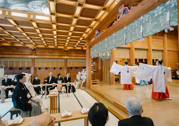 日本庭園で仲睦まじく見つめ合う、白無垢の花嫁と紋付袴の新郎の全身写真。