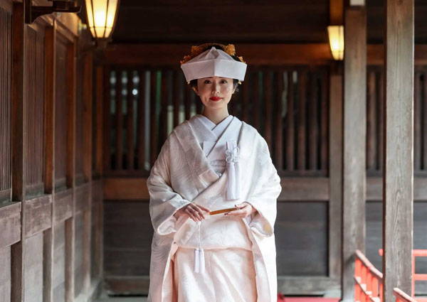 屋根付きの回廊に立つ、白無垢に綿帽子姿の花嫁