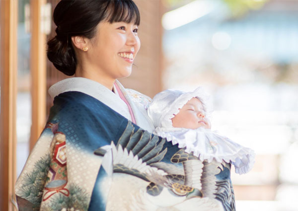 お宮参りの着物姿で、祝い着の赤ちゃんを抱いて微笑む母親
