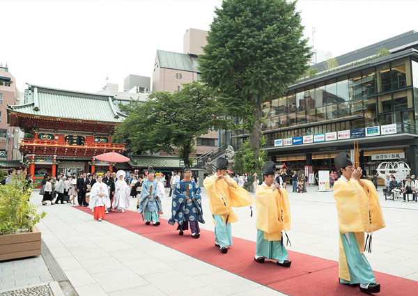朱塗りの門を背に、赤い絨毯を敷いた境内を神職を先頭に進む参進の列