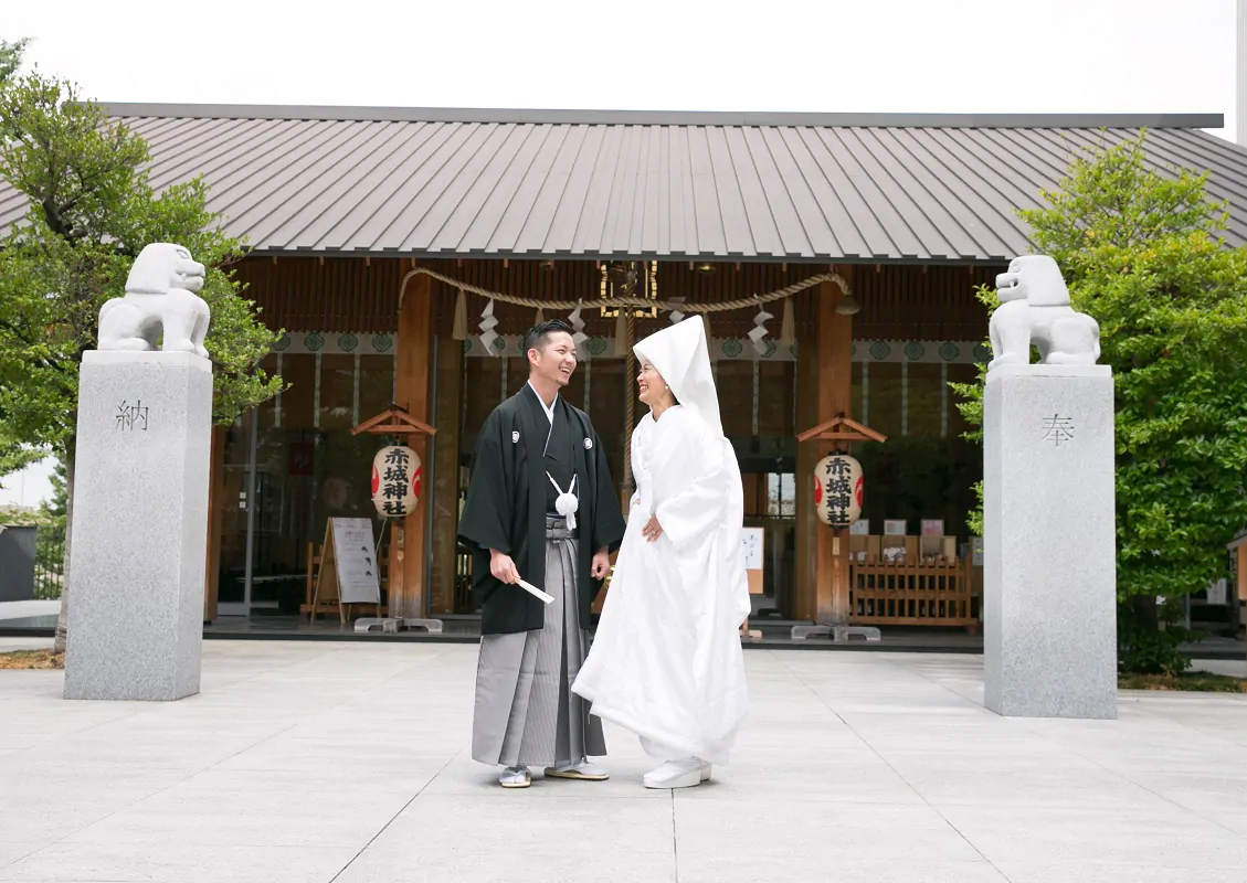 狛犬が並ぶ社殿前で向かい合う、綿帽子に白無垢の新婦と紋付袴の新郎
