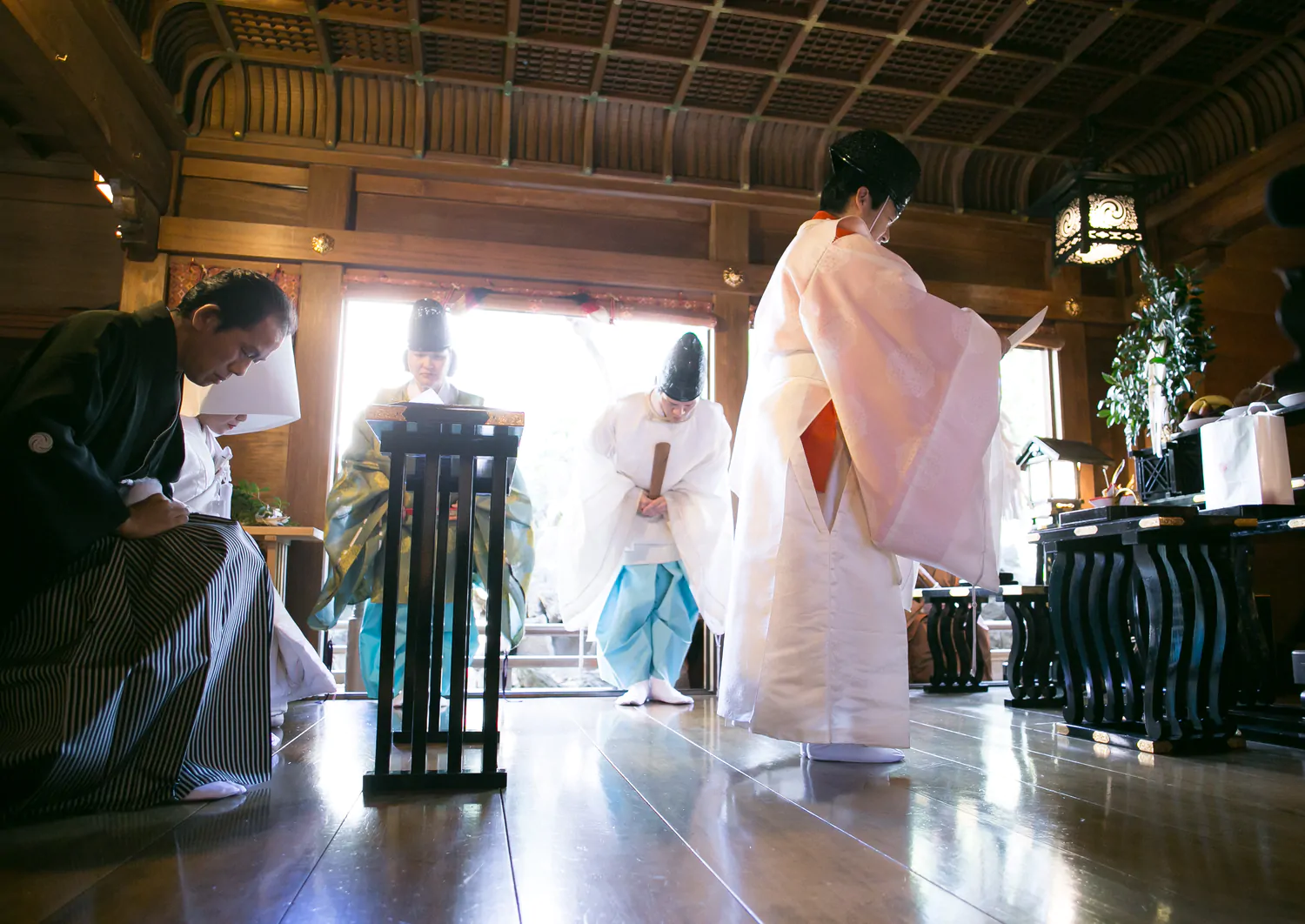 社殿の中で神職が祝詞を奏上し、頭を下げる紋付袴の新郎と白無垢の新婦