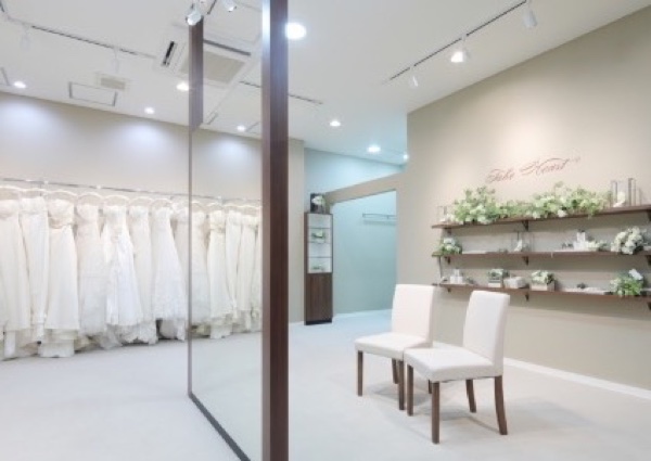 ウエディングドレスが並び、白い椅子と花を飾った棚がある明るいドレスサロンの店内