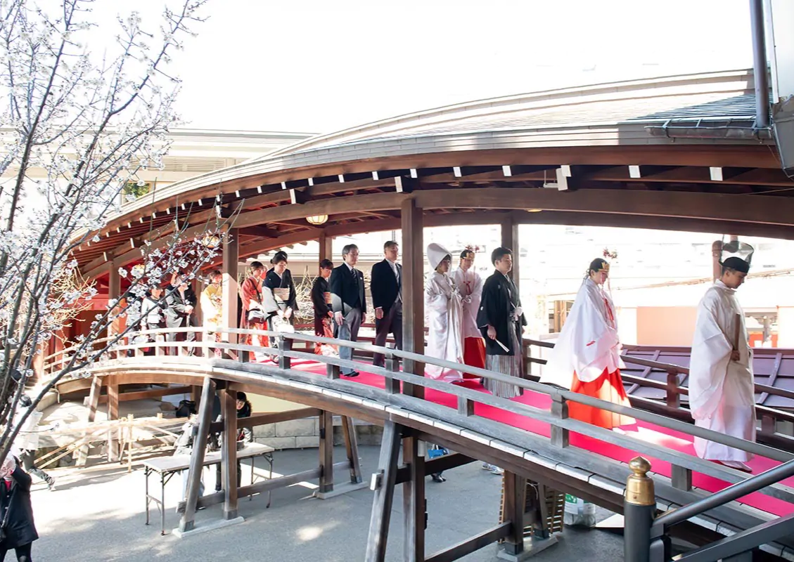 屋根のある太鼓橋を、神職と巫女に続いて花嫁と新郎、家族が列になって渡る参進