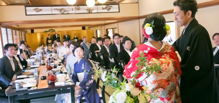 挙式後、色打掛の花嫁と紋付袴の新郎がご親族やゲストと囲む和室での会食