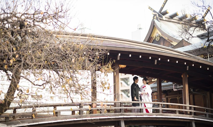 湯島天神の屋根付きの太鼓橋に立つ白無垢と紋付袴の新郎新婦