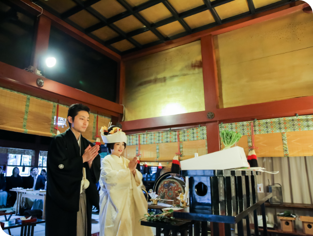 神前に供え物をし、手を合わせる新郎新婦